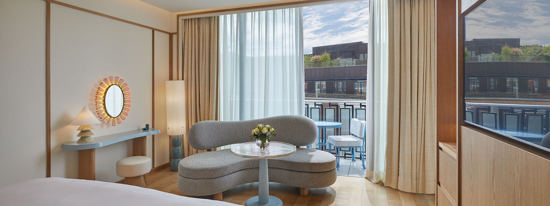 Curved grey and modern sofa with glass coffee table in front, placed in front of balcony with open glass doors and al fresco furniture